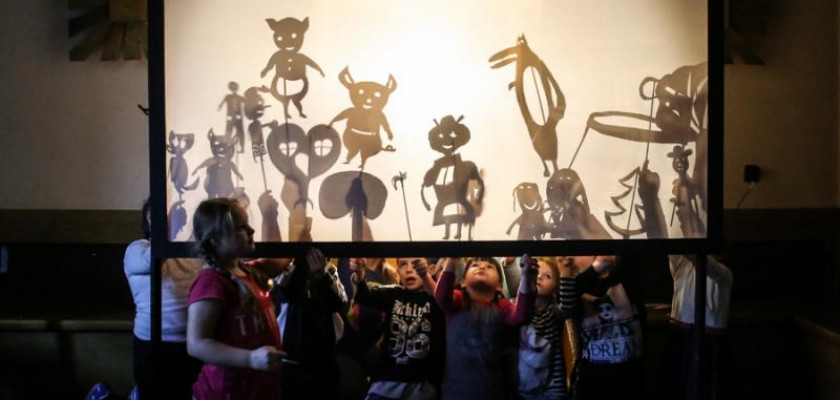 Zdjęcie przedstawia dzieci z kukiełkami postaci filmowych, pokazujących ich cienie na podświetlonympłótnie