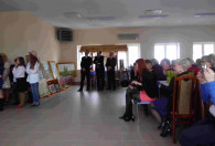 trzech mężczyzn w garniturach stoi na sali pełnej kobiet podczas obchodów dnia kobiet