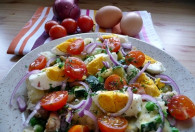 Zdjęcie przedstawia sałatkę z cukinią, pieczarkami i ziemniakami na talerzyku. Obok znajduje się pomidorki, cebula i jajka